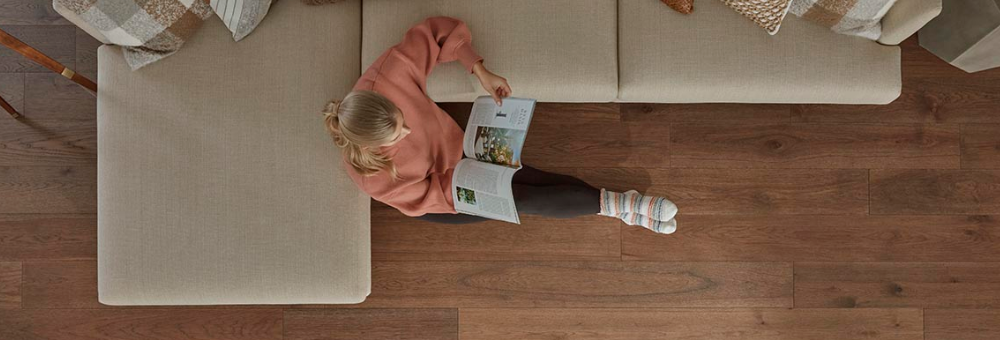 A woman sits on gorgeous, deep brown Mohawk engineered wood flooring reading a magazine.